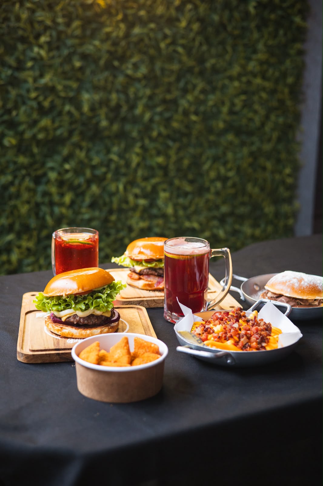 Mesa com hambúrgueres, fritas com cheddar e bacon e bebidas